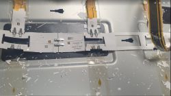 Zbliżenie na wnętrze urządzenia z elektroniką, z widocznymi taśmami LED i elementami montażowymi na metalowej powierzchni.