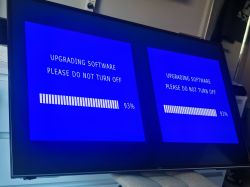 Telewizor z niebieskim ekranem „Upgrading software”, pasek postępu 93% widoczny podwójnie