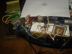 Prototypowy wzmacniacz lampowy z widoczną lampą elektronową, transformatorami i przewodami testowymi na biurku.