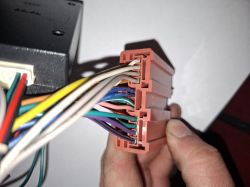 Zbliżenie na brązową wtyczkę instalacji radia samochodowego z kolorowymi przewodami, trzymaną w dłoni