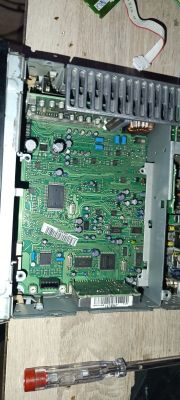Wnętrze radia samochodowego: zielona płytka PCB z elementami i złączem taśmy u góry.