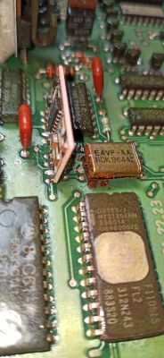 Zbliżenie na płytę drukowaną z różnymi komponentami elektronicznymi, w tym kilka układów scalonych i element oznaczony jako E4VF-AA NDK8644.