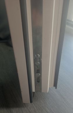 Zbliżenie na metalowy element ryglujący w ramie drzwi lub okna