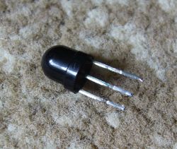 Three-pin sensor or IR receiver with a black housing, lying on a light surface.