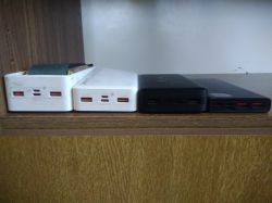 Four power banks side by side on a wooden shelf, front view showing USB ports