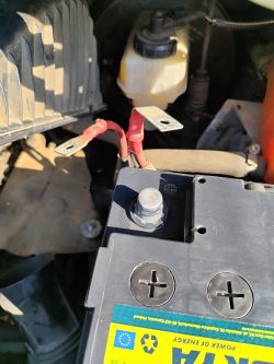 Nowy akumulator z widocznym zaciskiem mocowania i starymi klemami w samochodzie.