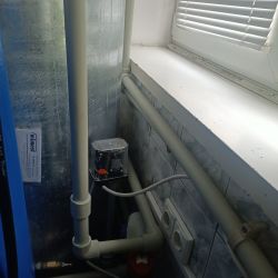Instalacja hydrauliczna w pomieszczeniu z rurami i urządzeniem pod oknem.