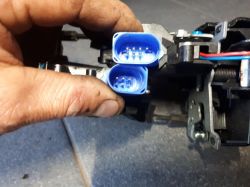 Ręka trzymająca dwa niebieskie złącza elektryczne zamka samochodowego z różną liczbą pinów.