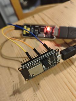 ESP32 module connected to USB-UART converter with jumper wires on a wooden surface