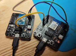Two electronic development boards connected with jumper wires on a wooden surface