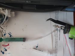 DIY Printer Cleaning Kit On the table is a makeshift printer head cleaning kit composed of a green syringe, a tube, and a multi-tool.