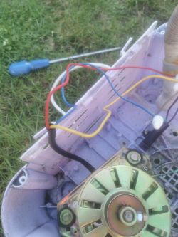 Silnik z kilkoma luźnymi przewodami w plastikowej obudowie, widoczny śrubokręt i trawa w tle.