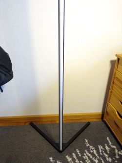 Modern vertical LED floor lamp on carpet next to wooden drawer unit