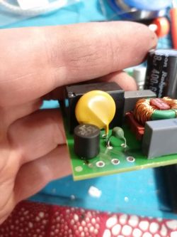 Płytka elektroniczna trzymana w ręce z widocznymi elementami elektronicznymi, w tym okrągły żółty element.