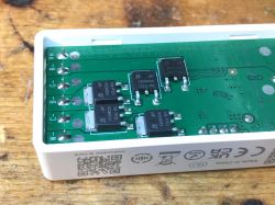 View of the interior of a white plastic electronic device with a mounted green circuit board and several black components.