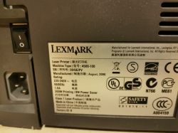 Zbliżenie na tabliczkę znamionową drukarki Lexmark z informacjami o modelu, zasilaniu i certyfikatach.