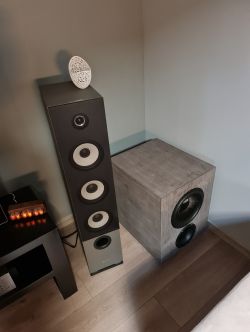 Subwoofer DIY obok kolumny głośnikowej w pokoju.