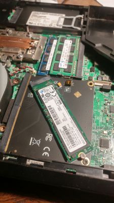 Otwarty laptop z zamontowanym dyskiem NVMe na adapterze.