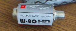 Zbliżenie na wzmacniacz liniowy OPTICUM W-20 HD z metalową obudową i złączami F, leżący na drewnianym blacie.