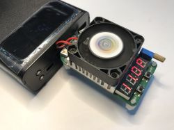 Power bank connected to an electronic load with cooling fan and LED display on a white surface