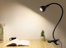 Lampka z klipsem oświetlająca otwartą książkę na drewnianym biurku