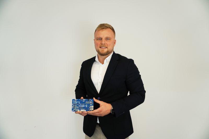 Man in a suit holding a blue Unisystem electronic board.