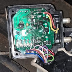 Płytka drukowana układu elektronicznego z kolorowymi przewodami i widocznymi elementami elektronicznymi w czarnej obudowie.