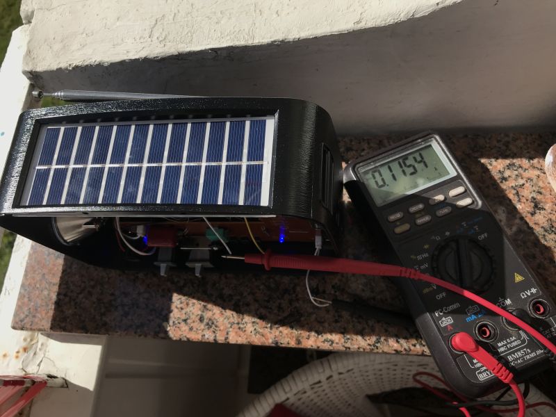 Radio z panelem solarnym mierzone miernikiem cyfrowym pokazującym prąd 0.1154 A