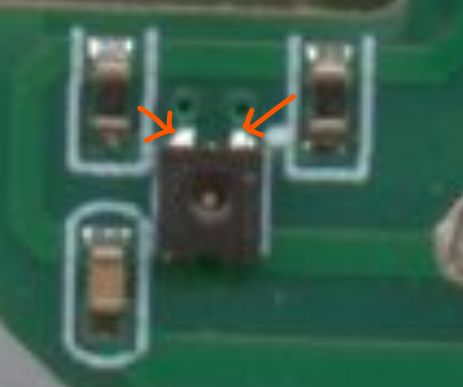 Close-up of a green PCB section with a small black component and two orange arrows pointing at it.