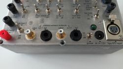 Panel kontrolny przystawki do pomiaru wzmacniaczy audio z przełącznikami i złączami wejściowymi/wyjściowymi.