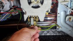 Ręka trzymająca odłączony przewód w maszynie z widocznymi połączeniami elektrycznymi i pinami.