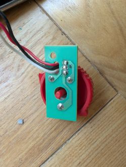 Potentiometer with PCB and Wires on Wooden Floor A red potentiometer with three attached wires and a PCB, lying on a wooden floor.