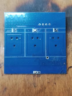 A blue printed circuit board (PCB) with visible tracks and mounting holes lies on a wooden surface.