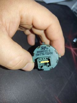 Ręka trzymająca szary element z oznaczeniami i złączem elektrycznym.