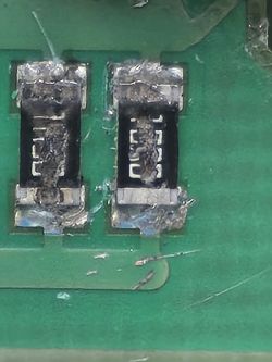 Zdjęcie dwóch uszkodzonych rezystorów na zielonej płytce drukowanej.