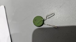 Zielony warystor z wygiętymi końcówkami leży na szarej powierzchni.
