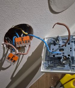 Open wall electrical box with wires and WAGO connectors next to a removed outlet mechanism