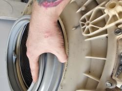 Zbliżenie na rękę montującą gumowy fartuch na plastikową obudowę bębna pralki.