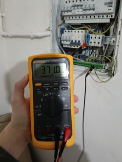 Multimetr Fluke 87 V pokazujący oporność 371,0 omów, trzymany przed rozdzielnicą elektryczną.