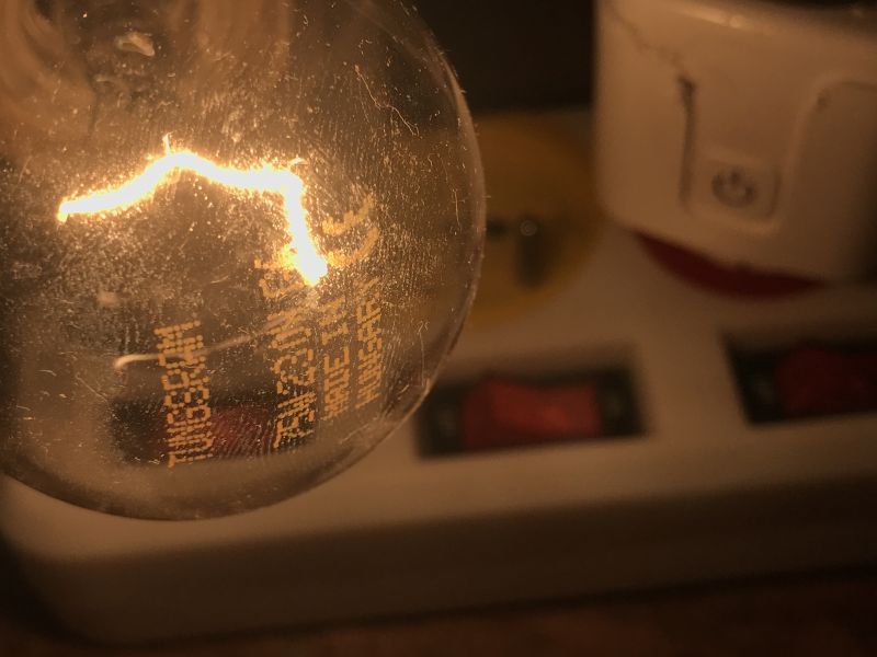 Light Bulb with Visible Filament Light bulb with visible filament and markings, power strip in the background.