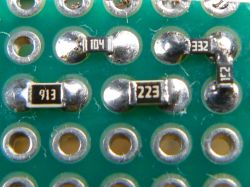 Close-up of a prototyping board with through-holes and several soldered SMD resistors