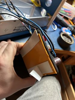 Hand holding a yellow enclosure piece with wires; S-1200-60 power supply in the background