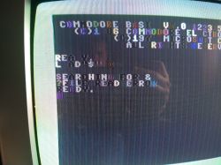 Zbliżenie ekranu Commodore C128 z przekłamanym, wielokolorowym tekstem i artefaktami graficznymi.
