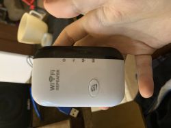Osoba trzyma w dłoni biało-czarny wzmacniacz sygnału WiFi z napisem WiFi REPEATER i przyciskiem WPS.