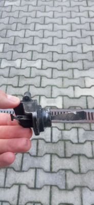 Osoba trzymająca uszkodzony element samochodu przed kostką brukową.