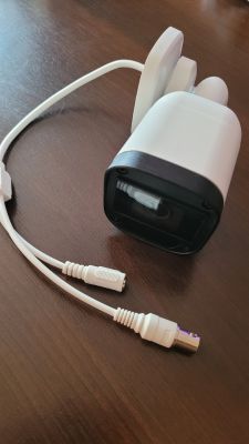 Kamera monitoringu z kablami do podłączenia, leżąca na drewnianym stole.