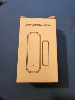 Door/Window Sensor Box A white cardboard box labeled Door/Window Sensor with a schematic outline of a door/window sensor set on a blue surface.