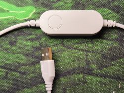 LED Controller with Button A white device with a button and USB cable, resting on a green mat.