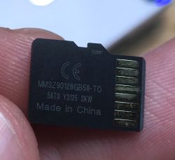 Close-up of a black microSD card with technical markings held between fingers