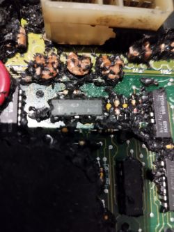 Spalona płyta PCB z uszkodzonymi elementami i śladami stopionego materiału.